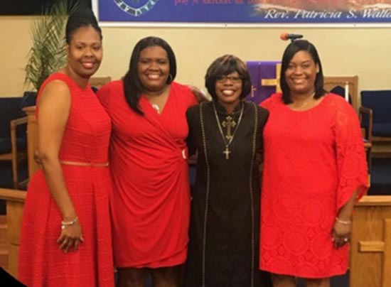 three women dressed in red and one in black standing and smiling for a photo